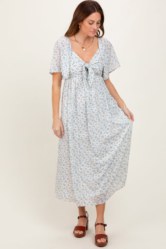 woman wearing a light blue floral maxi dress with short sleeves and a waist tie, standing on a neutral background