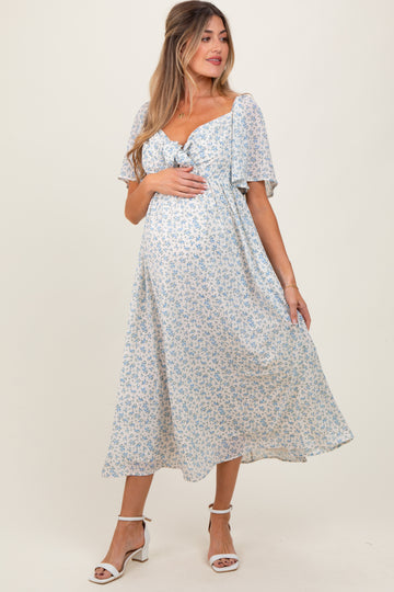 woman wearing a light blue floral maternity dress with a tie front and flutter sleeves, showing baby bump