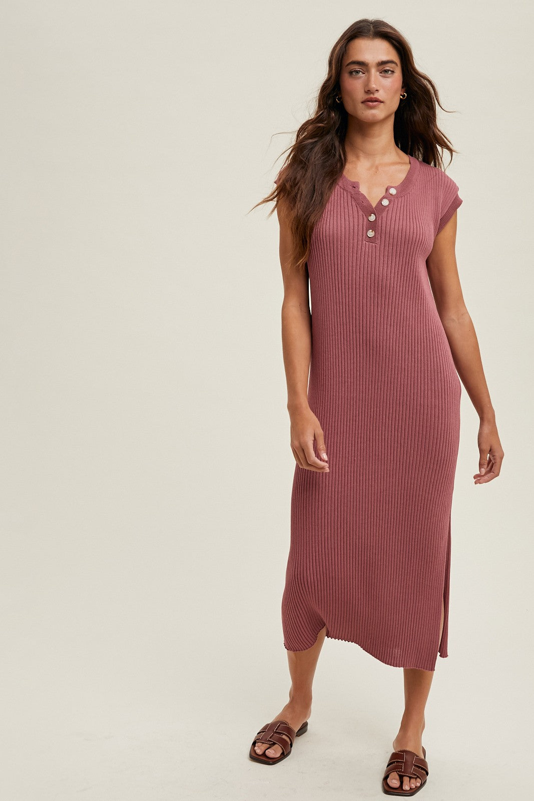 woman wearing a rust-colored ribbed midi dress with short sleeves and button details, standing against a neutral background