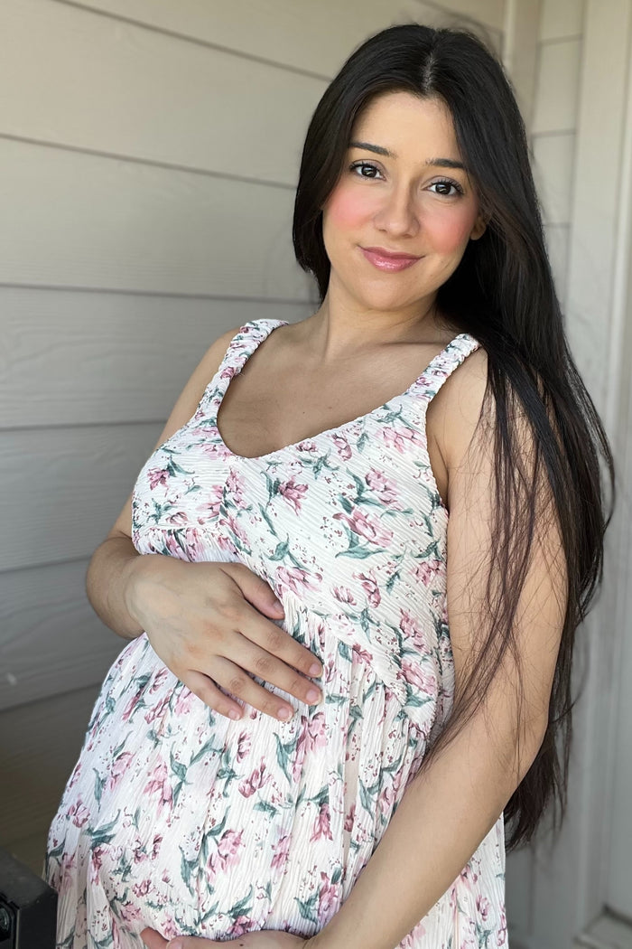 woman wearing a floral print maternity dress, gently holding her baby bump