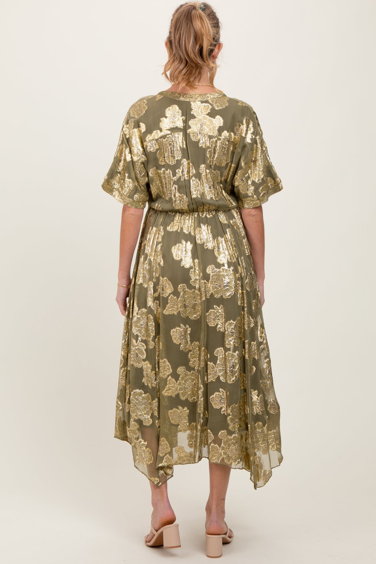 woman wearing a green floral maternity dress with gold detailing and a flowy hem, viewed from the back