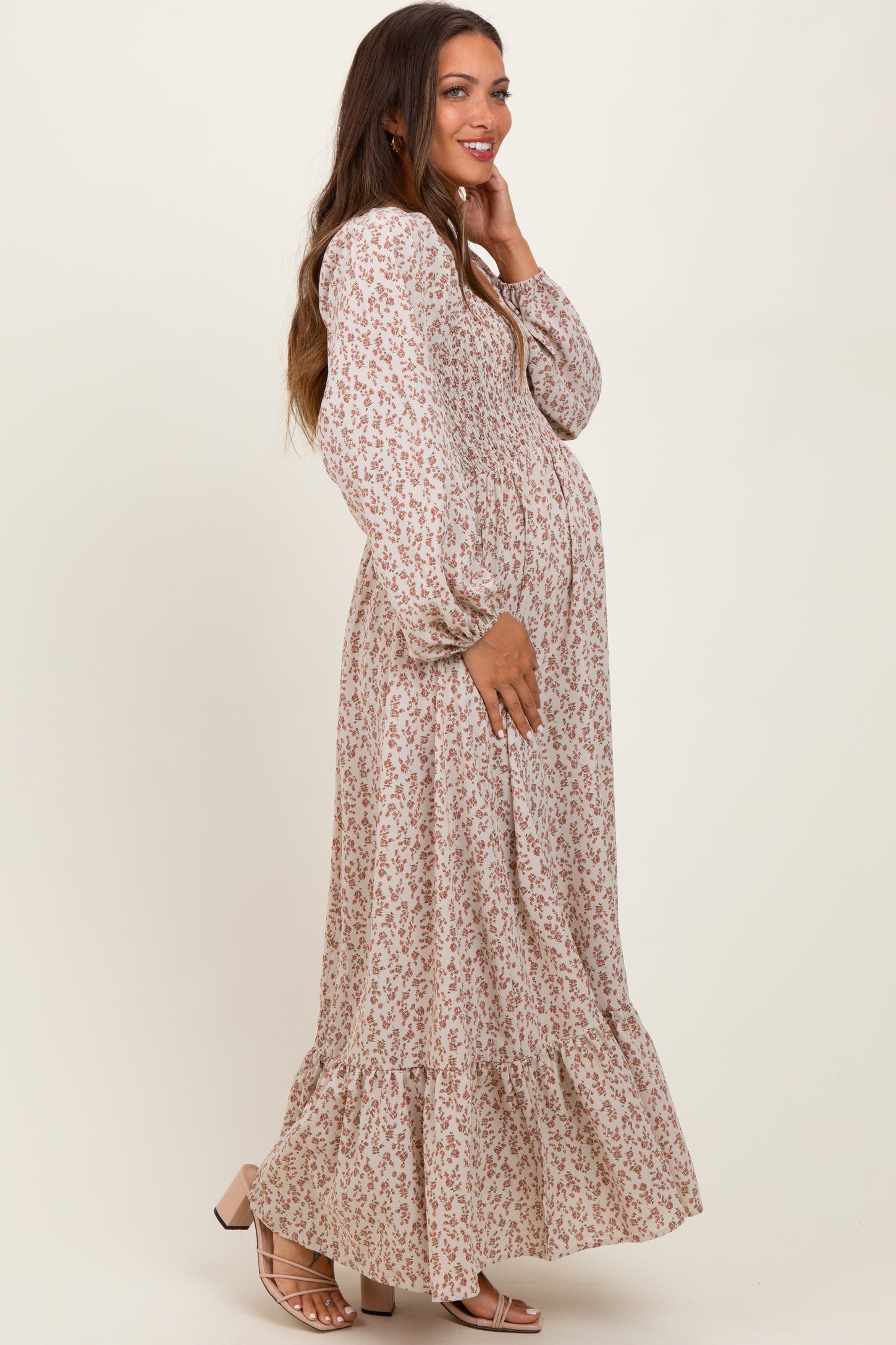 woman wearing a floral long sleeve maternity dress with a tiered skirt and holding her baby bump