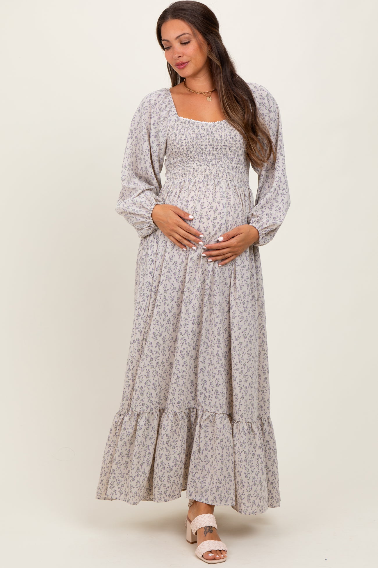 woman wearing a light floral print maternity dress with long sleeves and a tiered skirt, holding her baby bump