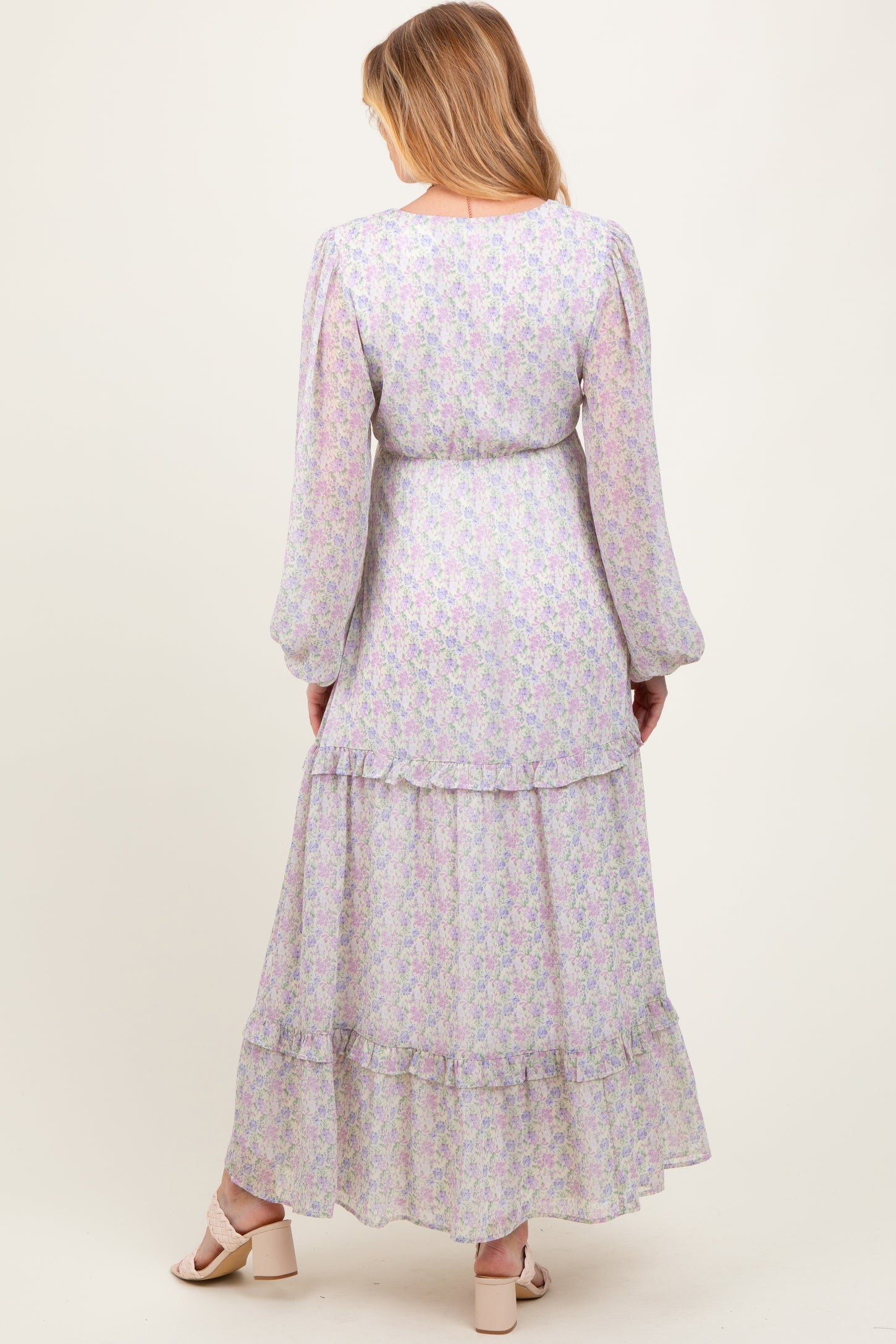 woman wearing a pastel floral long sleeve maternity maxi dress with a tiered skirt and tie waist detail
