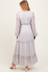 woman wearing a pastel floral long sleeve maternity maxi dress with a tiered skirt and tie waist detail