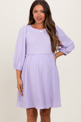 woman wearing a light purple maternity dress with long sleeves and a ruffled waistline, smiling at the camera