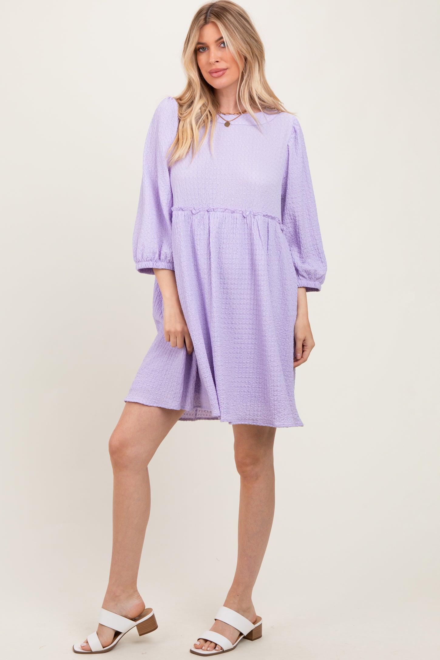 woman wearing a lavender puff sleeve dress with a gathered waist and a relaxed fit, paired with white block heeled sandals