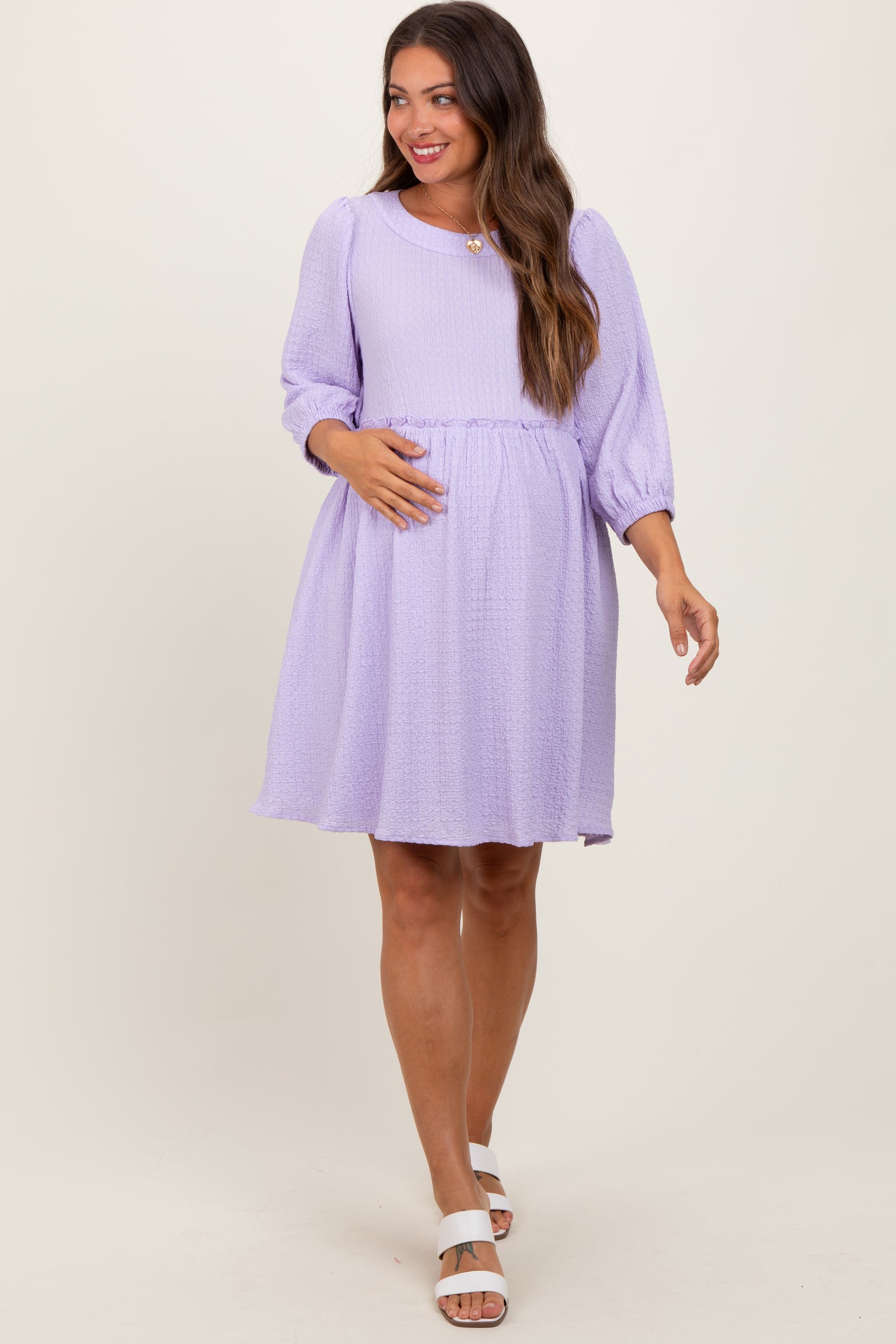 woman wearing a light purple maternity dress with a smocked waist and puff sleeves, holding her baby bump