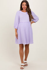 woman wearing a lavender maternity dress with three-quarter sleeves and a smocked waist, showing her baby bump