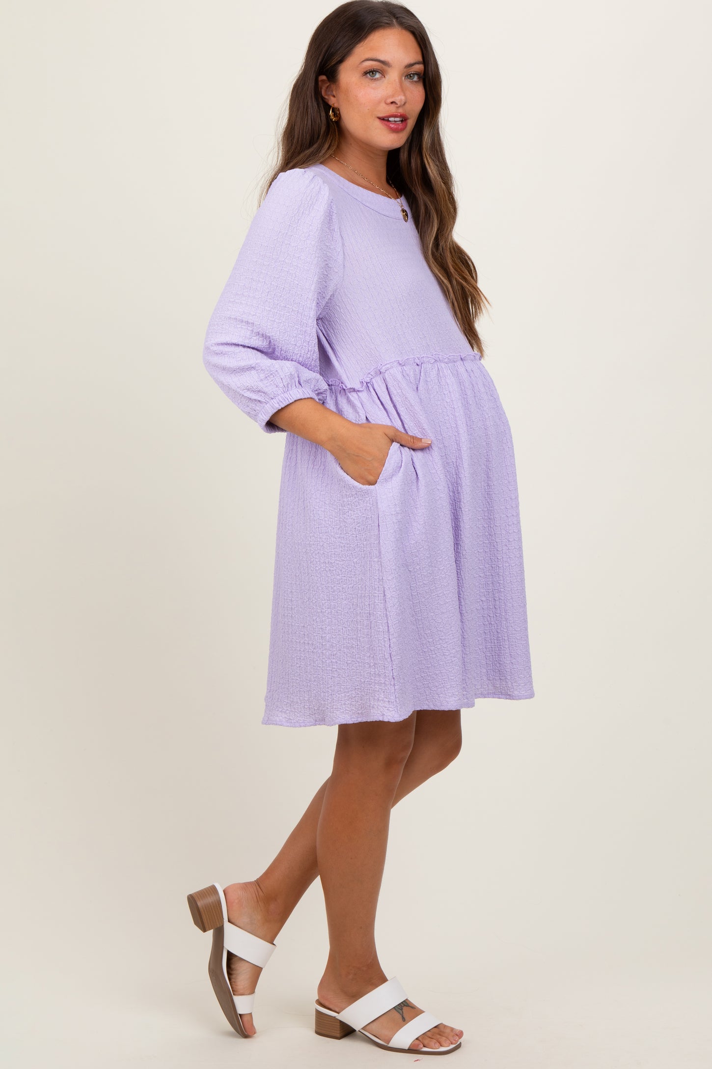 woman wearing a lavender maternity dress with three-quarter sleeves, waist tie, and side pockets, showing her baby bump