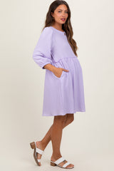 woman wearing a lavender maternity dress with three-quarter sleeves, waist tie, and side pockets, showing her baby bump