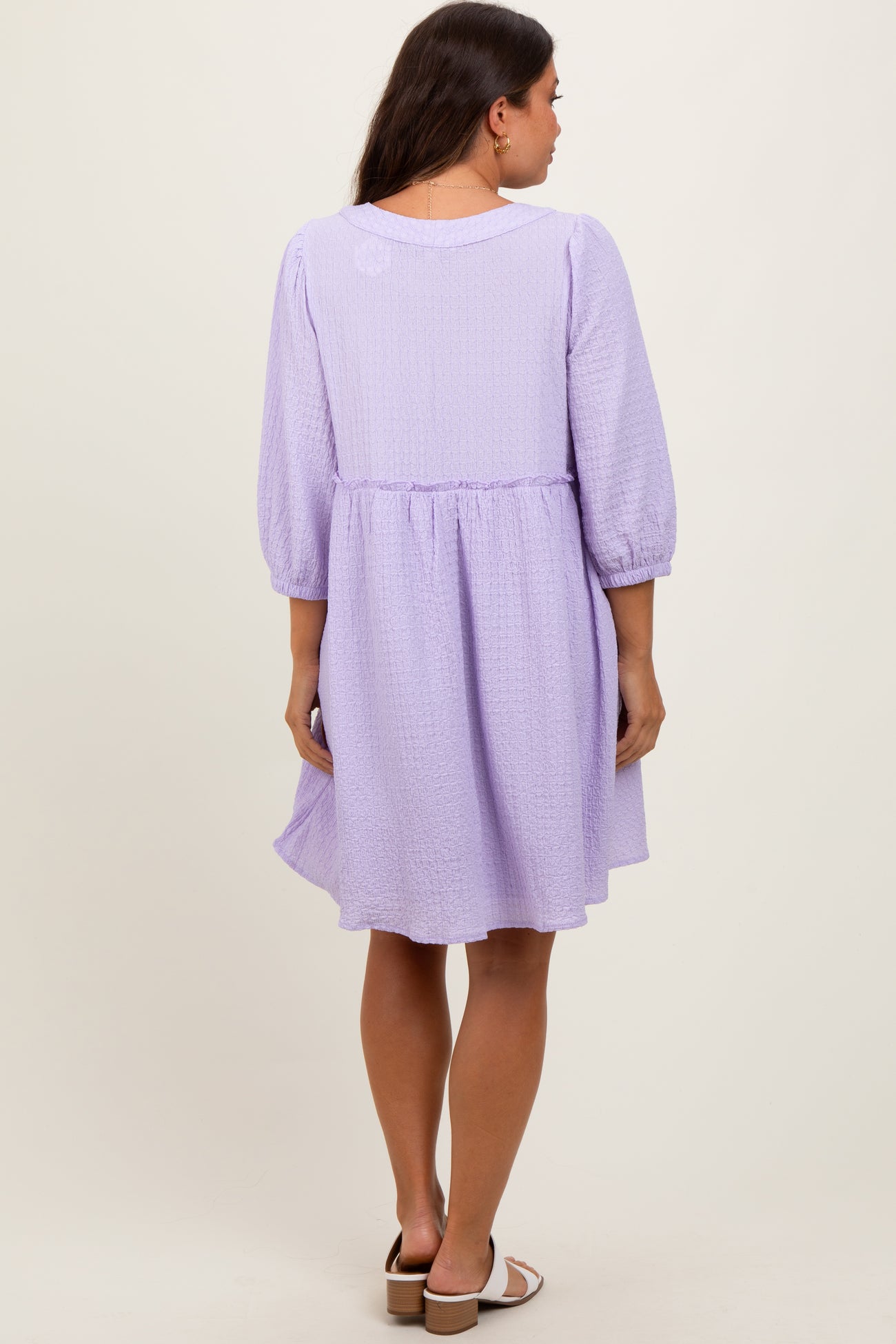 woman wearing a lavender maternity dress with three-quarter sleeves and a cinched waist, showing a relaxed fit