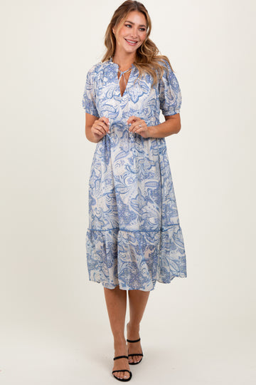 woman wearing a blue paisley print midi dress with puff sleeves and a tiered skirt, standing and smiling