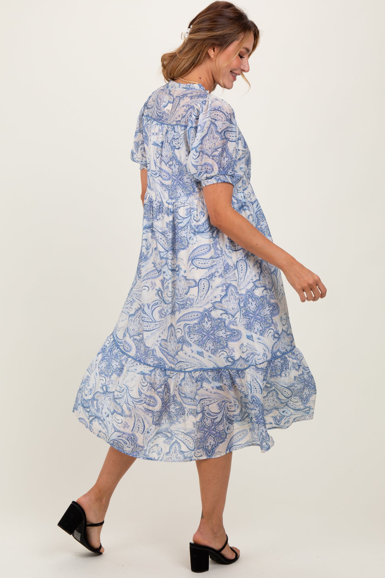 woman wearing a blue paisley print midi dress with puff sleeves and a tiered skirt, walking and smiling