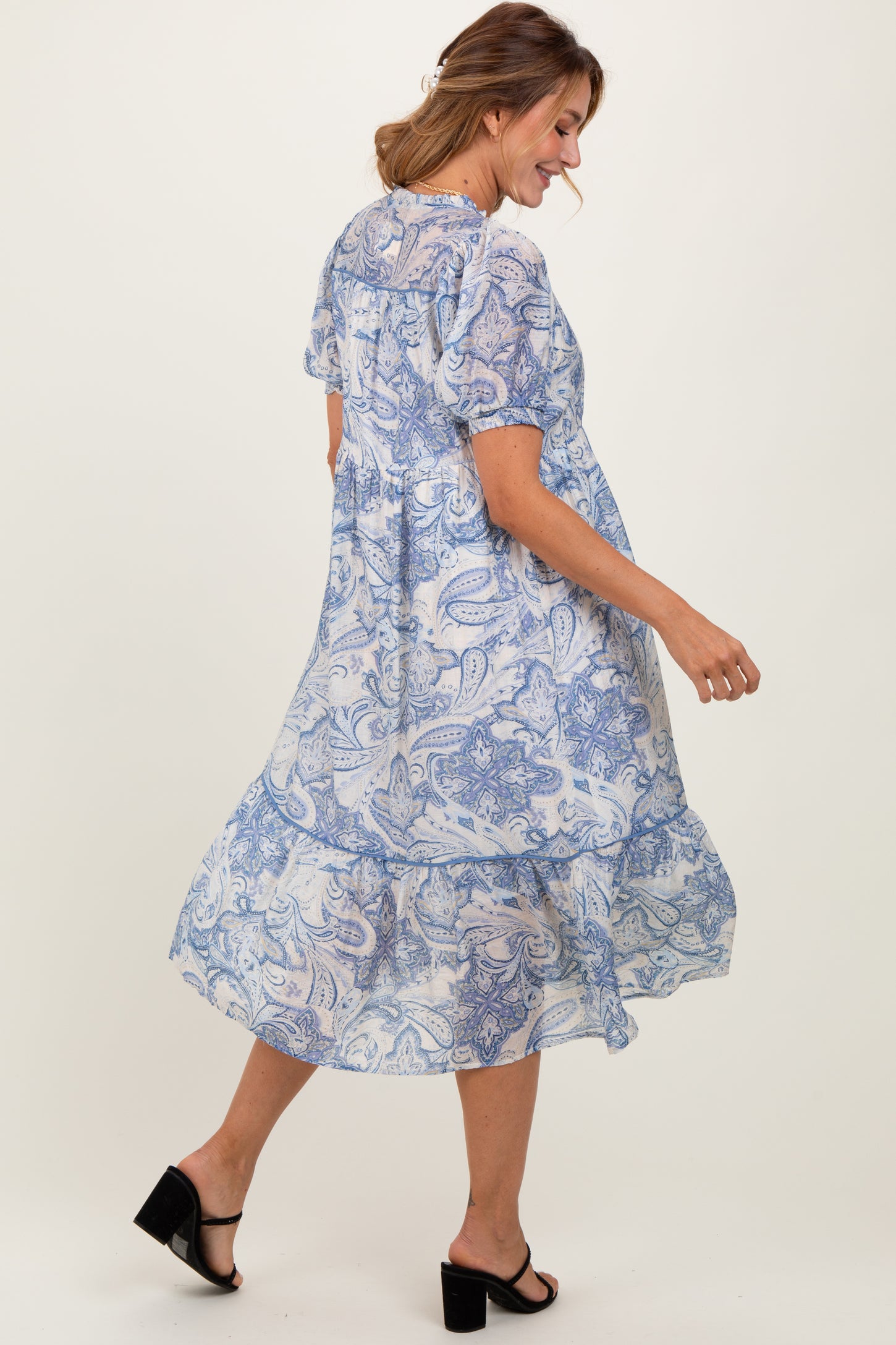 woman wearing a blue paisley print midi dress with puff sleeves and a tiered skirt, walking and smiling