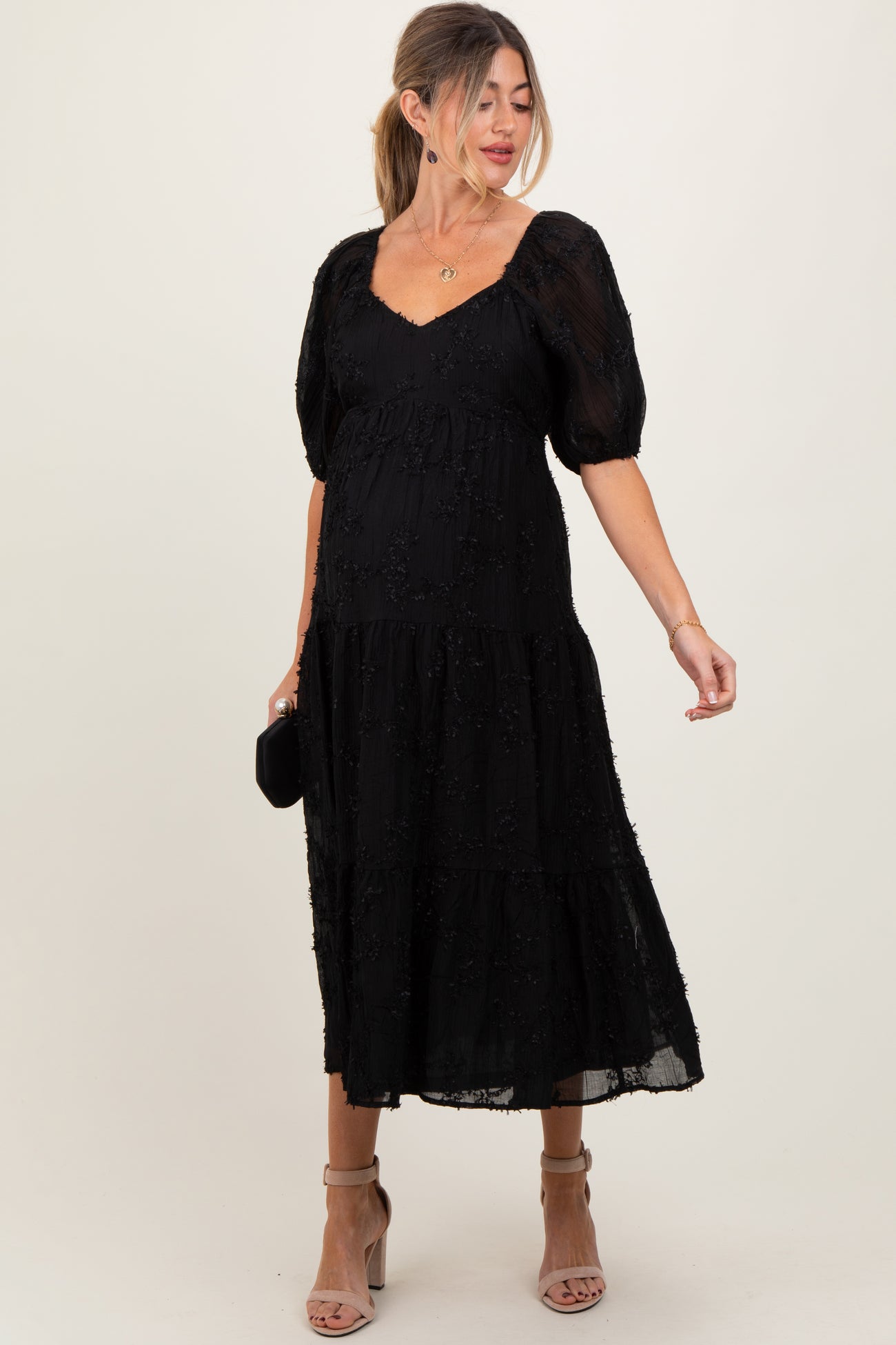 woman wearing a black puff sleeve maternity dress with a tiered design and visible baby bump