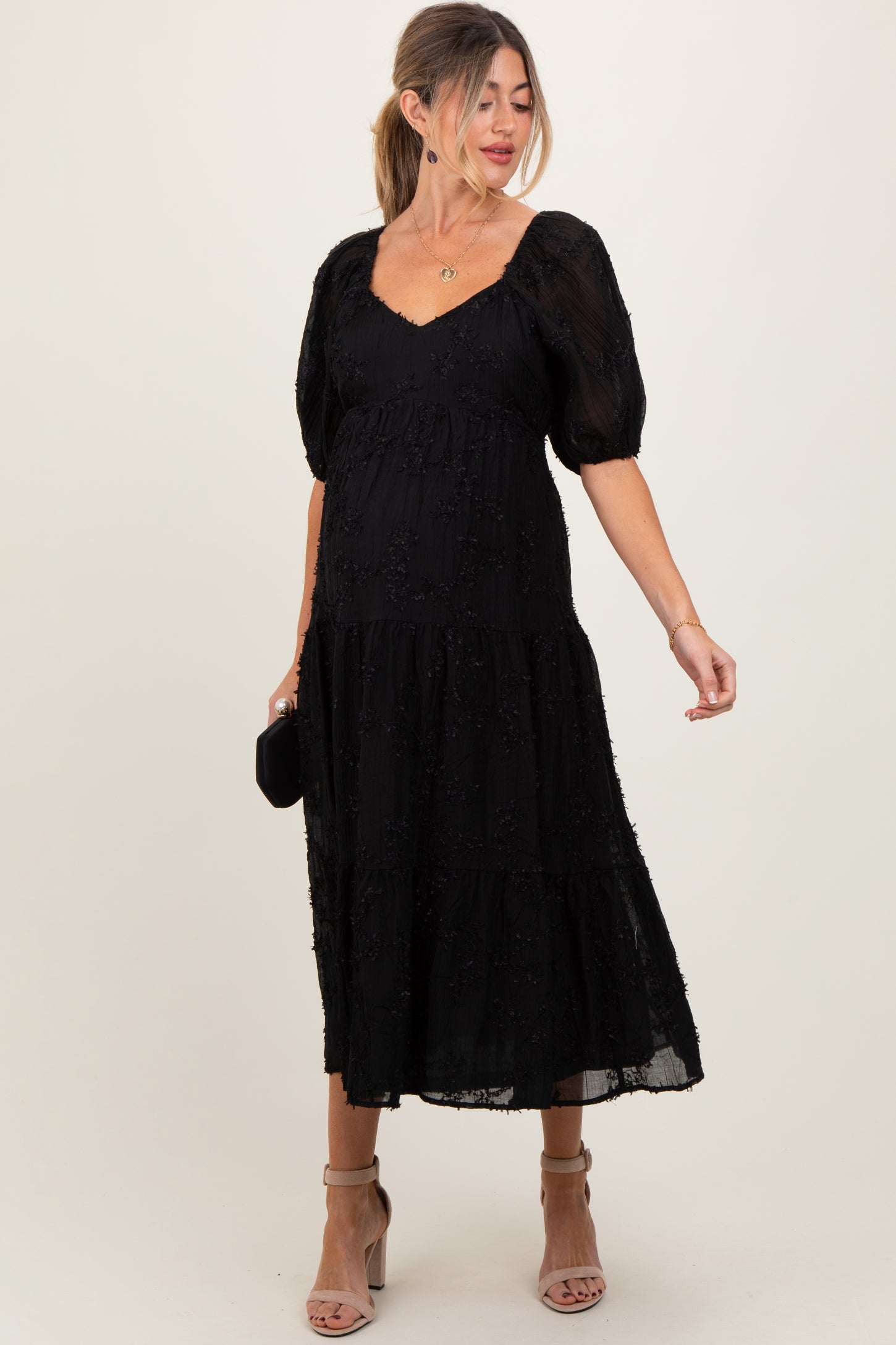 woman wearing a black puff sleeve maternity dress with a tiered design and visible baby bump
