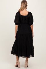 woman wearing a black puff sleeve maternity dress with tiered skirt and a square back, styled with nude heels