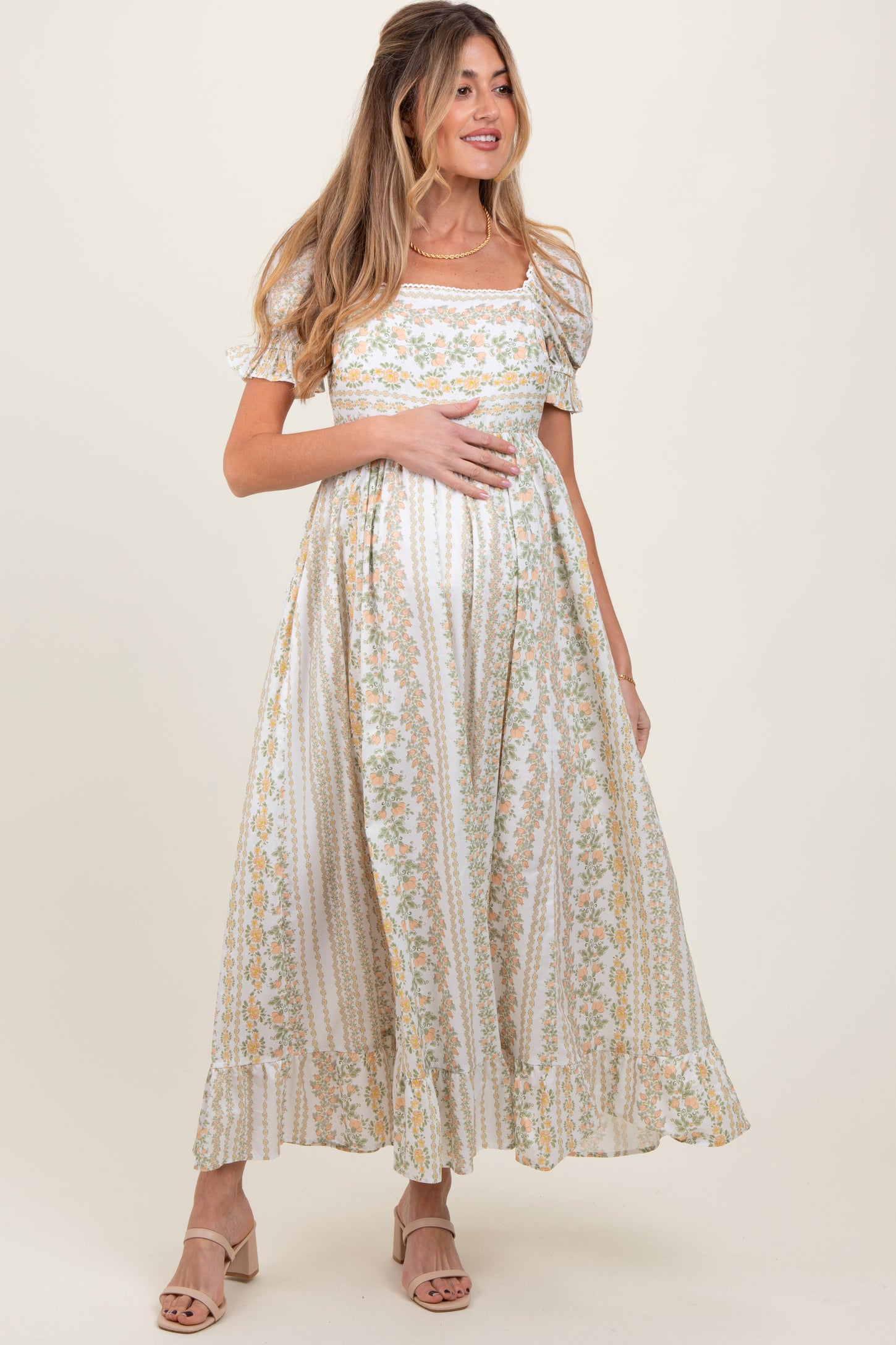woman wearing a floral print white maternity dress with short puffy sleeves and holding her baby bump