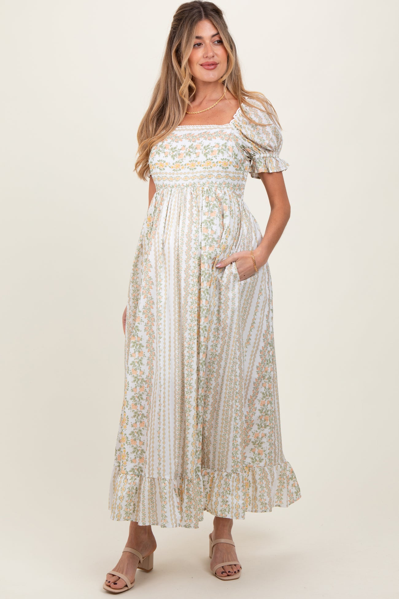 woman wearing a floral print white maternity dress with puff sleeves and pockets, showcasing her baby bump