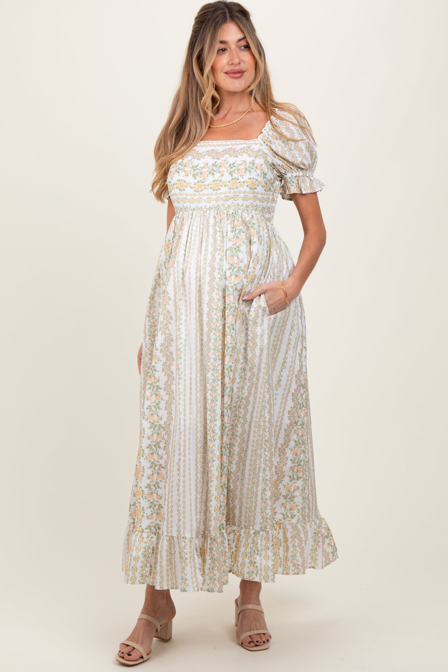 woman wearing a floral print white maternity dress with puff sleeves and pockets, showcasing her baby bump