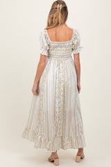 woman wearing a white maternity maxi dress with floral print and puff sleeves, showing her back with a smocked bodice