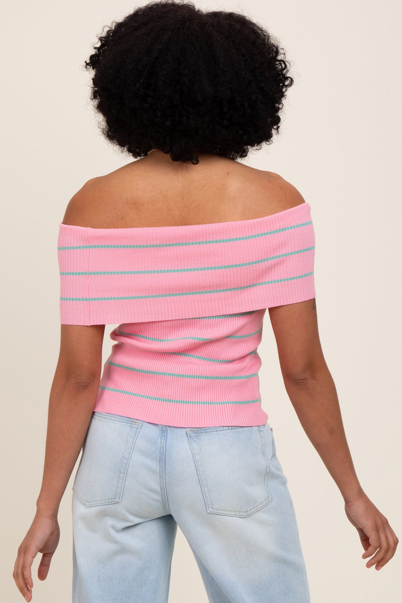 woman wearing a pink off-the-shoulder ribbed top with blue and white stripes and light wash baggy jeans