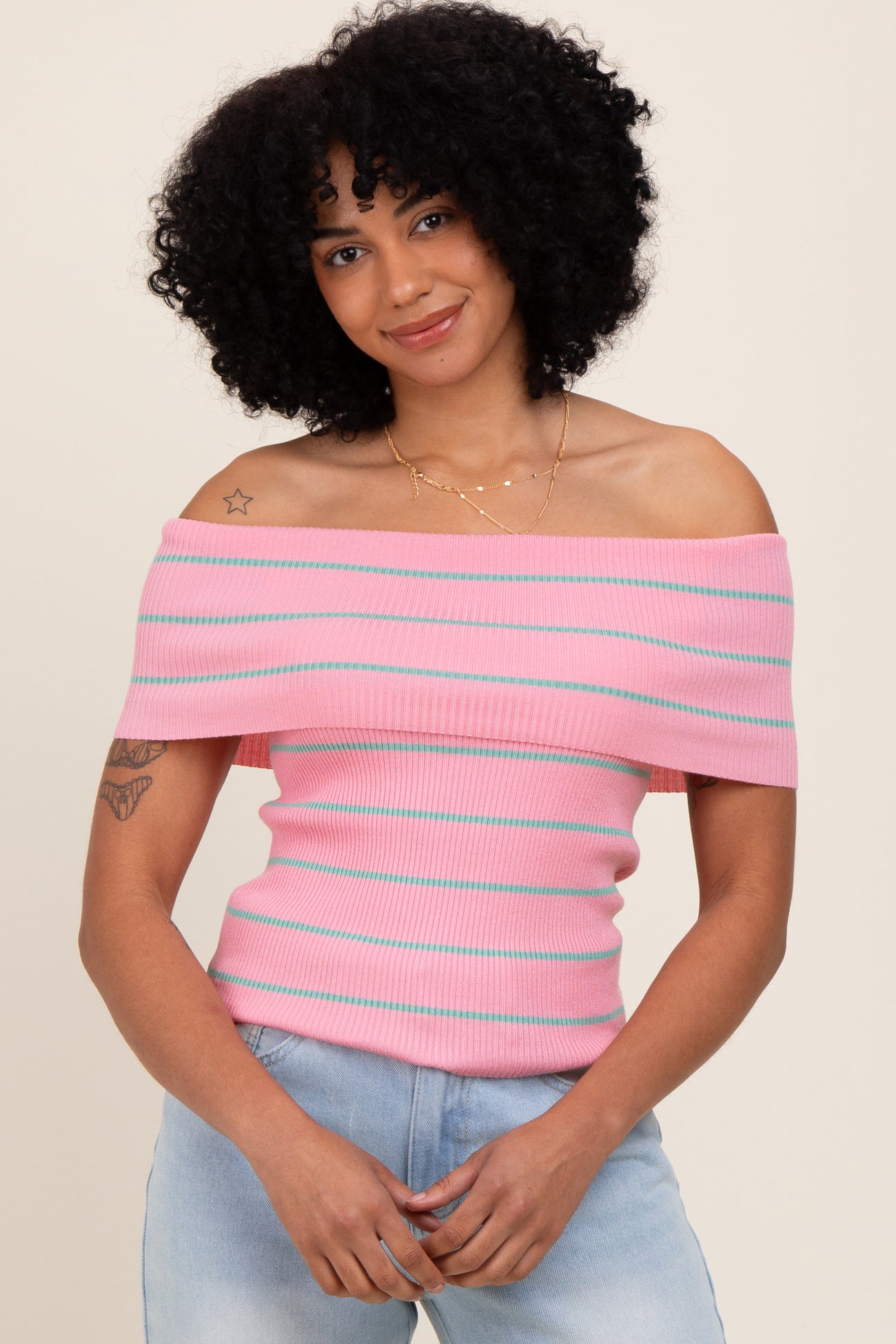 woman wearing a pink off-the-shoulder ribbed top with horizontal stripes and light blue jeans