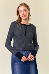 woman wearing a black and white striped long sleeve top with buttons and a scoop neckline paired with a denim skirt