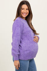 woman wearing a purple maternity sweater and showing her baby bump while smiling