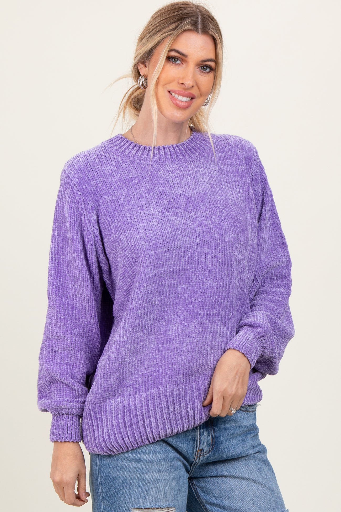 woman wearing a purple oversized sweater with ribbed details and long sleeves, smiling against a light background