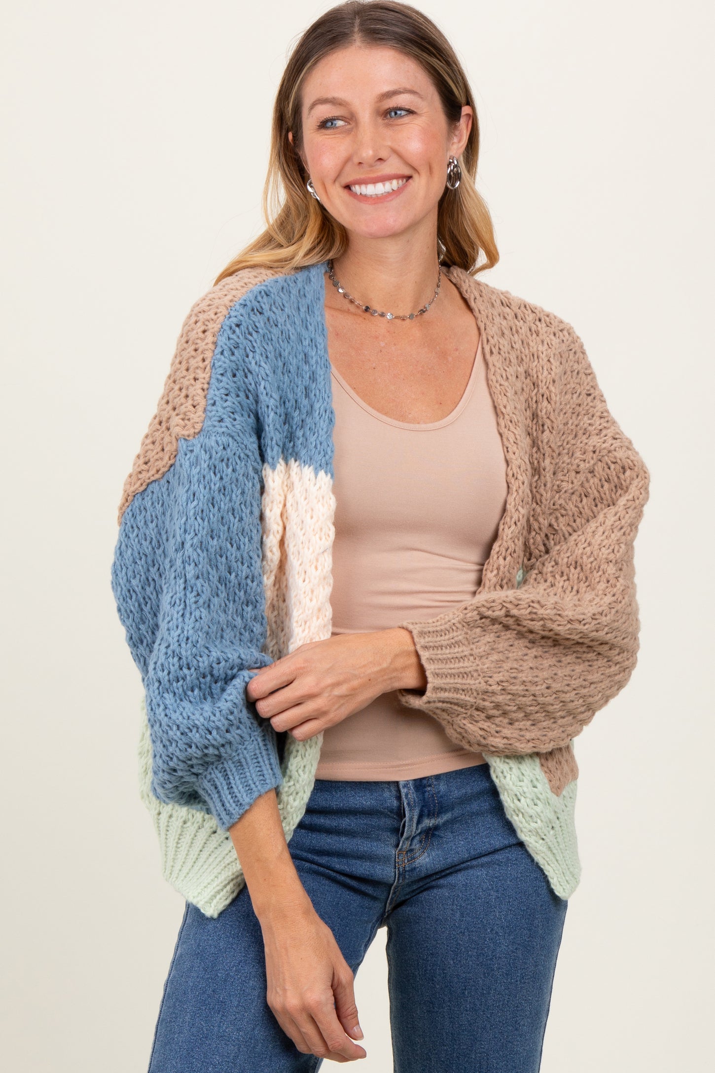 woman wearing a multicolored chunky knit cardigan over a beige top with blue, brown, and green sections
