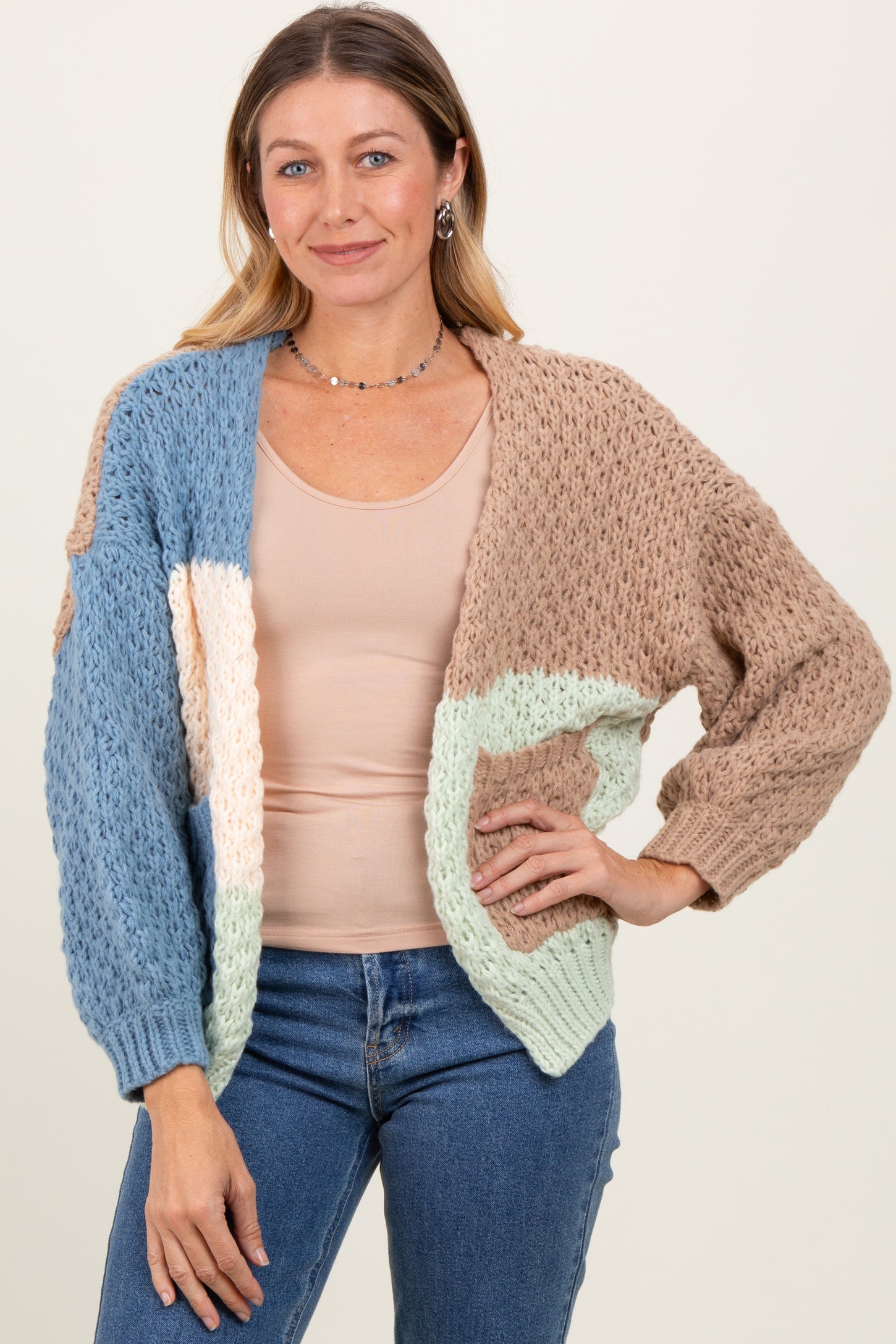 woman wearing a multi-colored knitted cardigan over a beige top with light blue and brown details, standing against a neutral background
