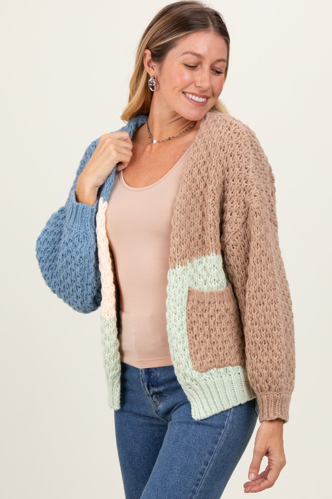 woman wearing a chunky knit cardigan in tan, blue, and mint with a pocket, paired with a nude tank top and jeans