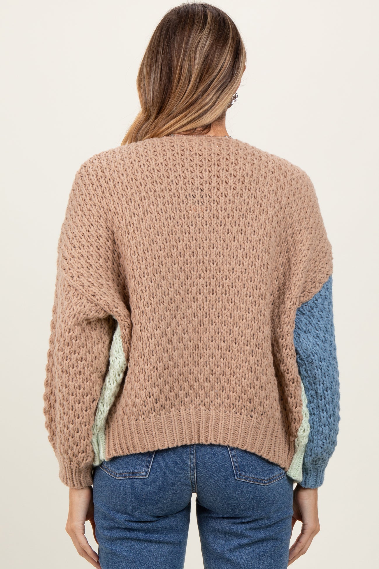 woman wearing a pastel color block knit sweater with a textured pattern and long sleeves, facing away from the camera
