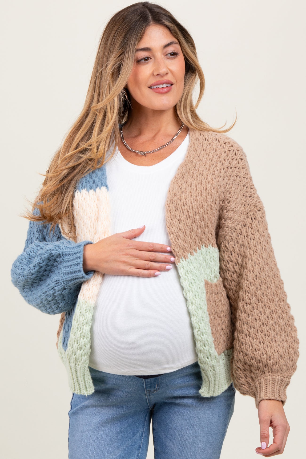 woman wearing a multicolored chunky knit maternity cardigan and holding her baby bump
