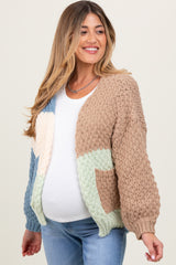 woman wearing a multi-colored knitted maternity cardigan and showing her baby bump