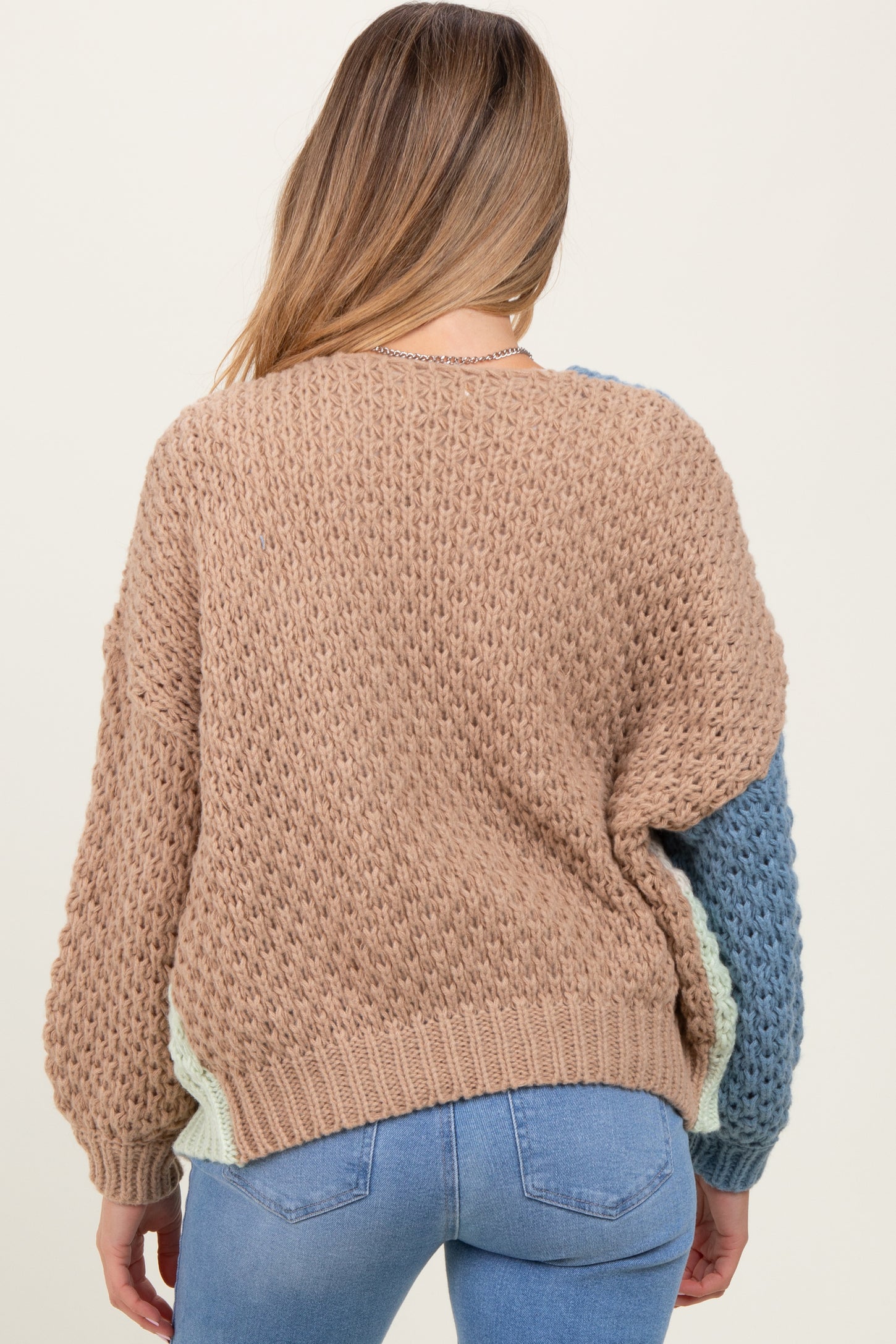 woman wearing a beige and blue knitted maternity sweater with a loose fit and oversized sleeves