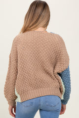 woman wearing a beige and blue knitted maternity sweater with a loose fit and oversized sleeves