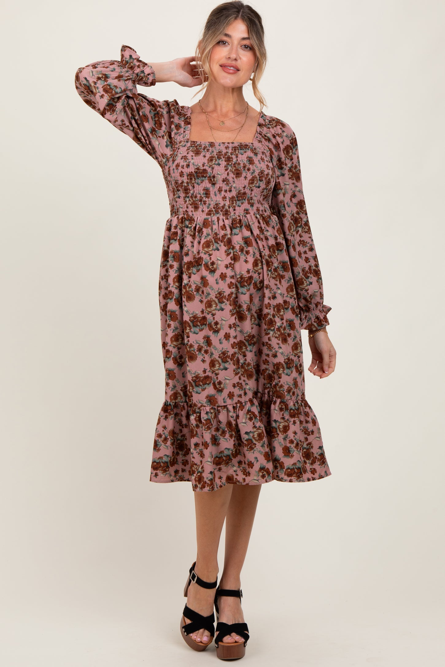 woman wearing a floral pink maternity dress with long sleeves and a tiered ruffle hem, showcasing a baby bump