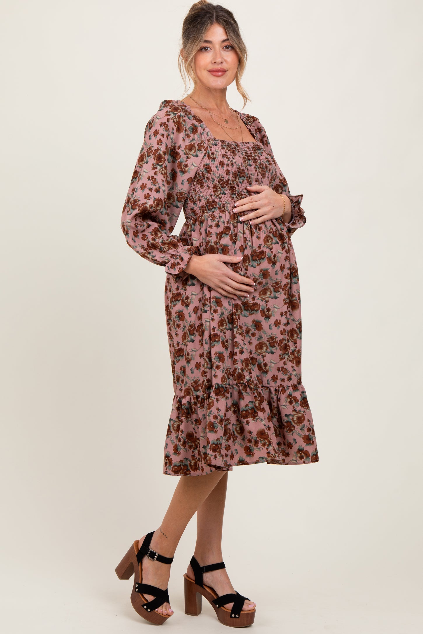 woman wearing a floral pink maternity dress with a smocked bodice and ruffled hem, holding her baby bump