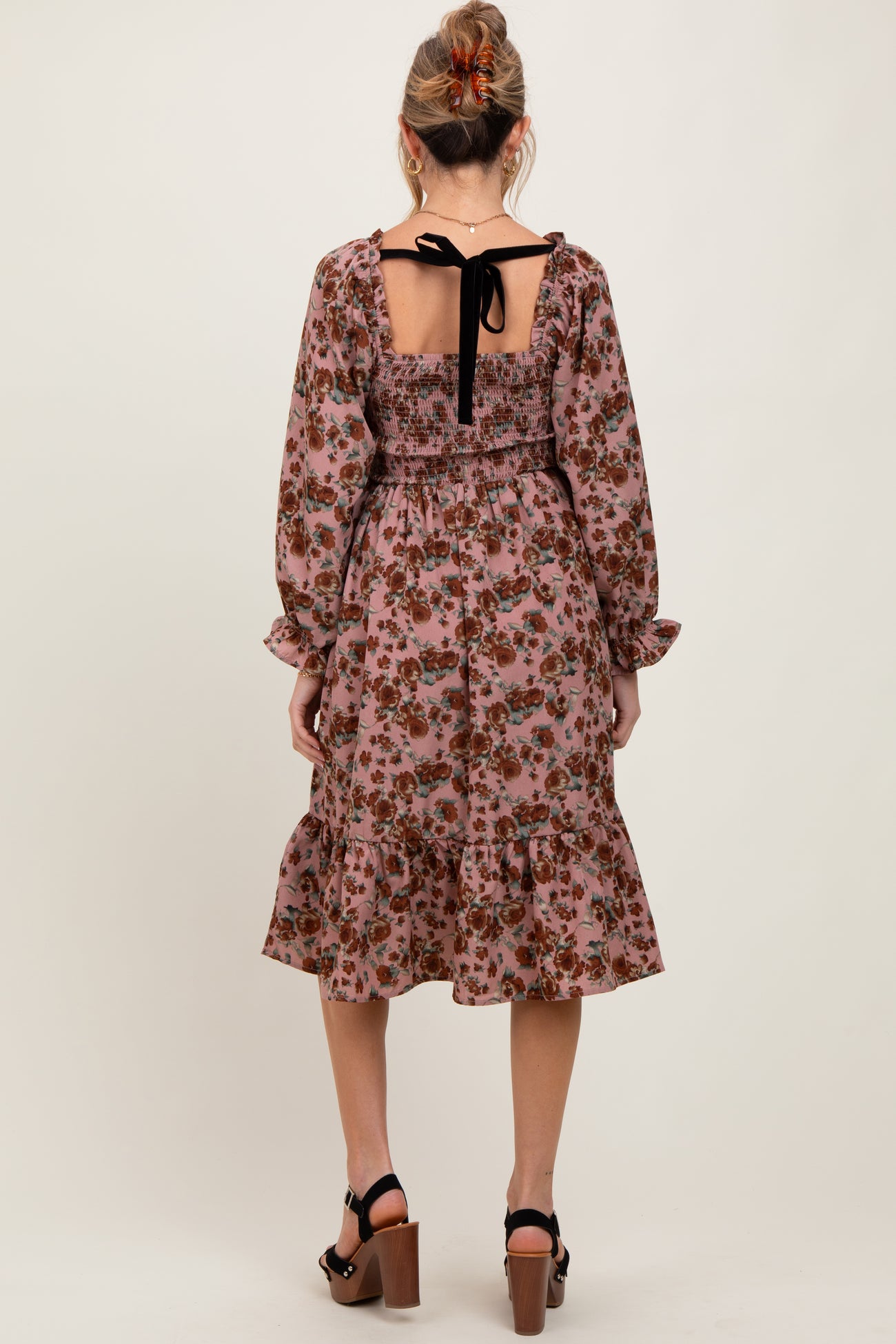 woman wearing a floral maternity dress with a smocked back and tie detail, featuring long sleeves and a ruffled hem