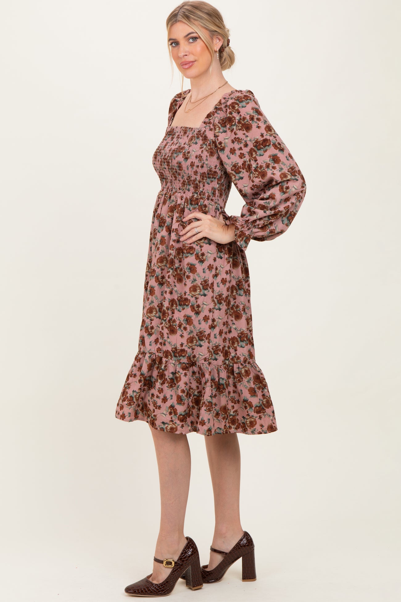 woman wearing a pink floral smocked midi dress with puff sleeves and a ruffled hem, standing in profile