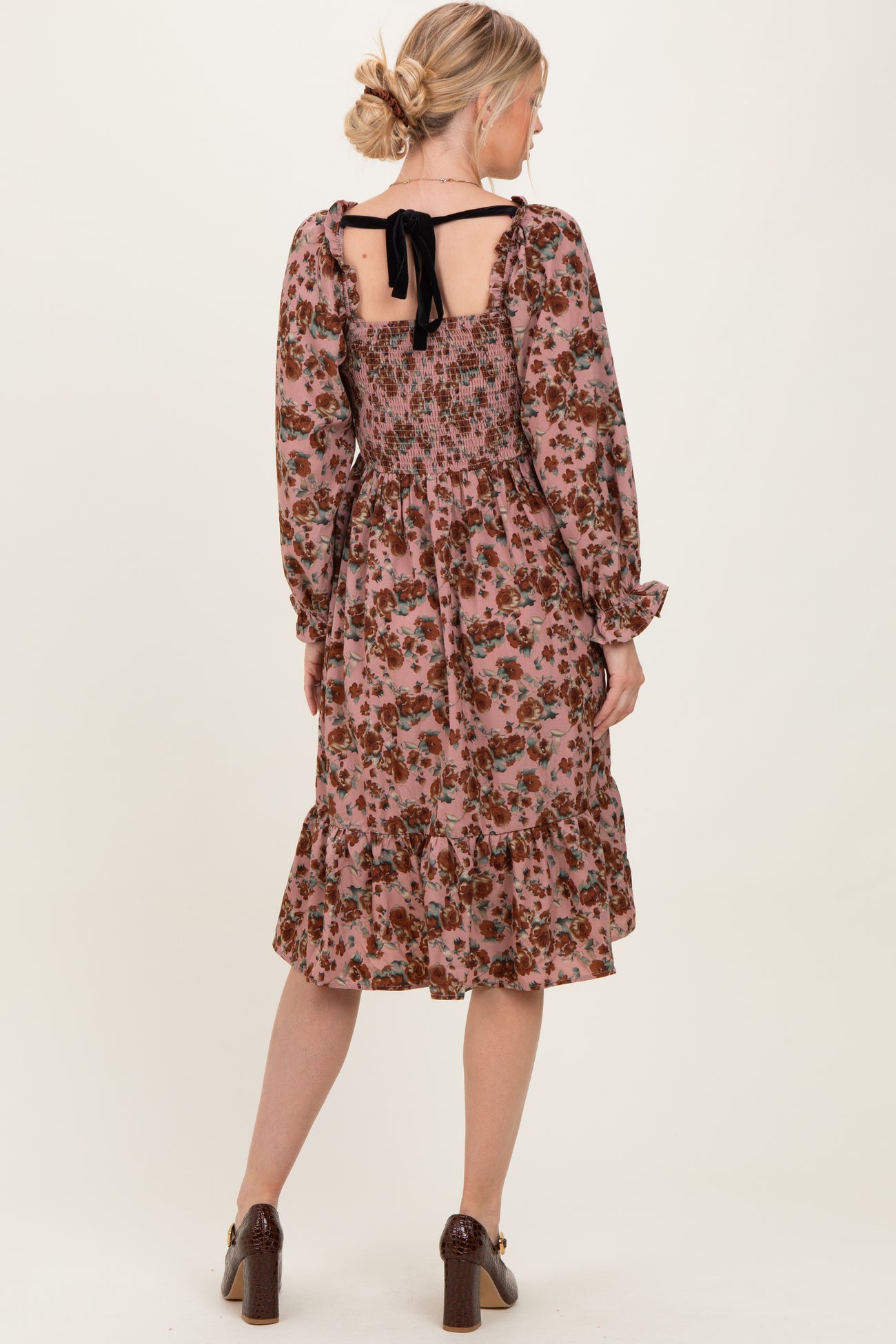 woman wearing a pink floral smocked midi dress with long sleeves and a tied open back detail