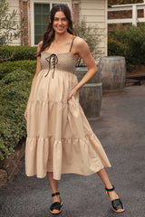 woman wearing a beige maternity dress with a tiered design and lace-up detail, standing with a visible baby bump