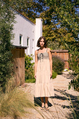 woman wearing a beige tiered maxi dress with a checkered bodice and adjustable tie detail, standing in a garden setting