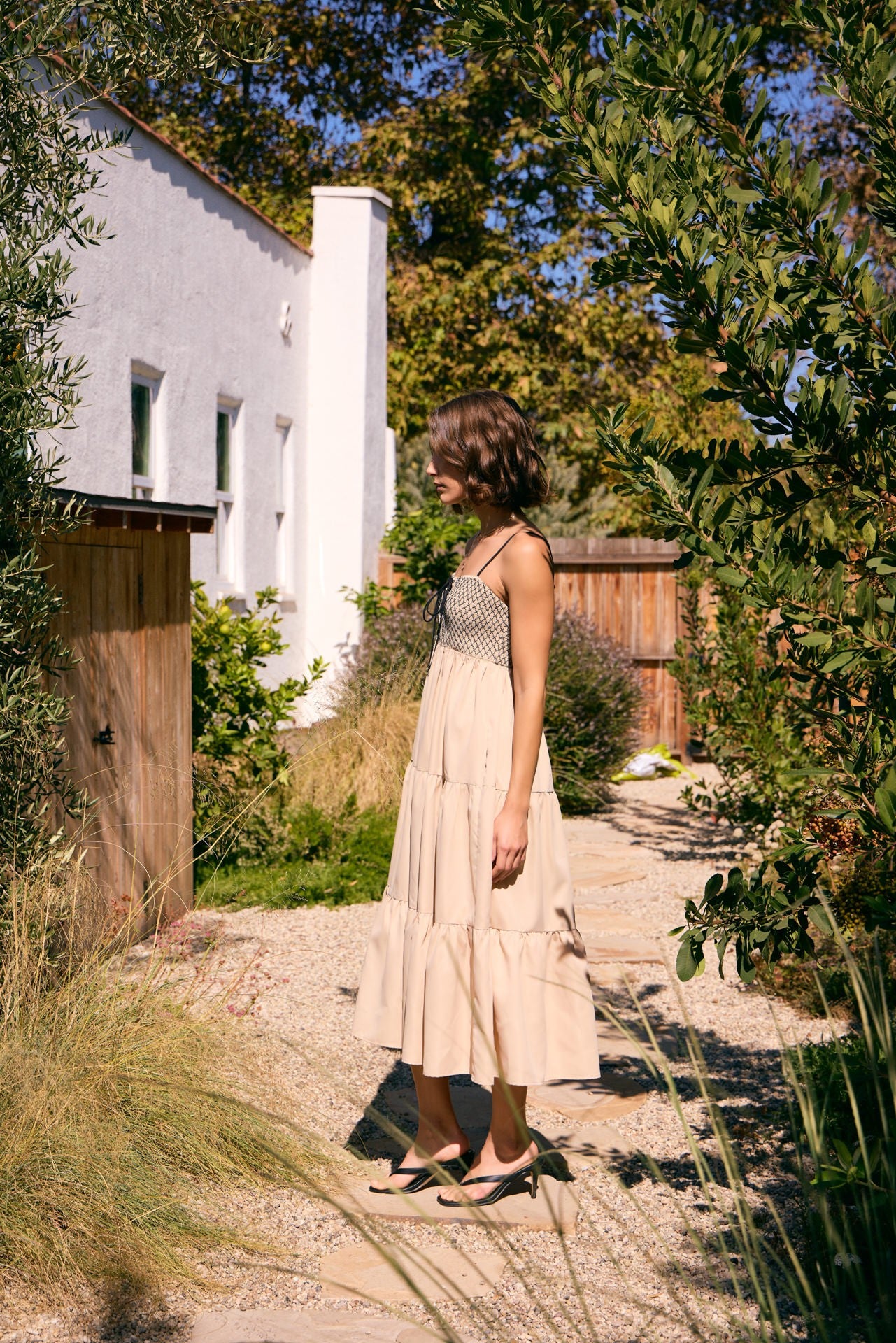 woman wearing a beige tiered maxi dress with a patterned bodice, standing in a garden setting
