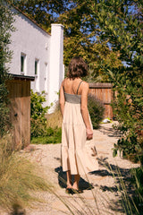 woman wearing a beige tiered maxi dress with a black checkered bodice, walking in a garden path