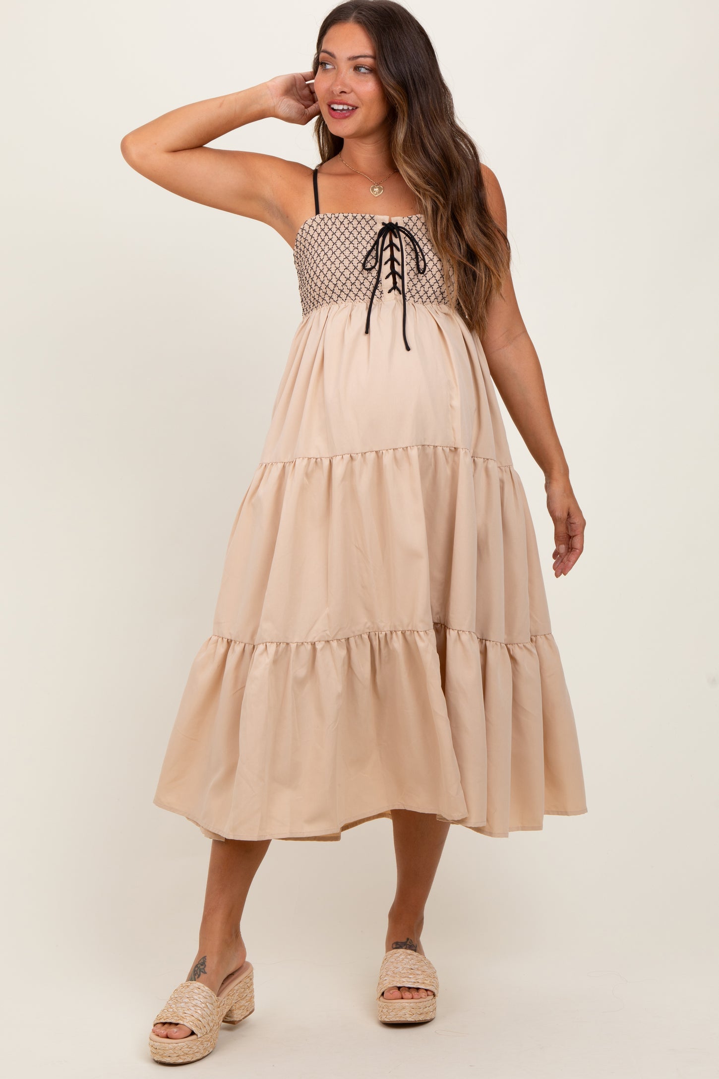 woman wearing a beige maternity dress with smocked bodice, tie detail, and tiered skirt, showing her baby bump