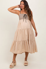 woman wearing a beige maternity dress with smocked bodice, tie detail, and tiered skirt, showing her baby bump